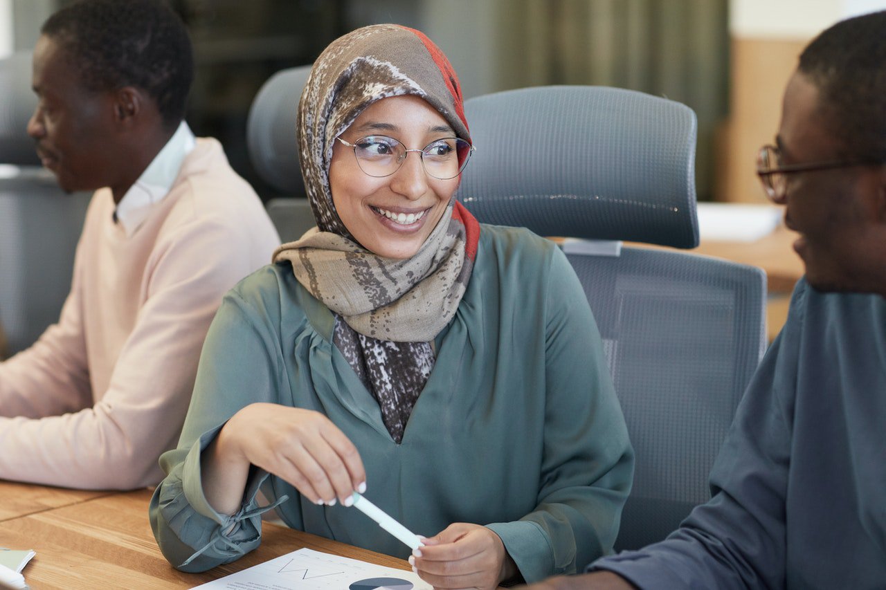Girl with a hijab in a conference room smiling at the man seat next to her.